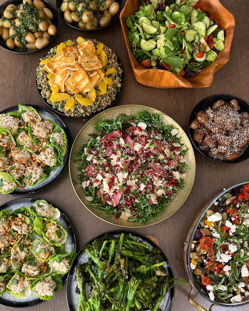 An abundant spread of gourmet salads, roasted vegetables, and hearty dishes displayed in rustic serving bowls on a wooden table.